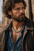 May include: A beaded necklace featuring a sequence of cylindrical turquoise-colored beads interspersed with small metallic gold-toned spacers and smooth black spherical beads, worn over a blue denim shirt and a distressed brown leather jacket.