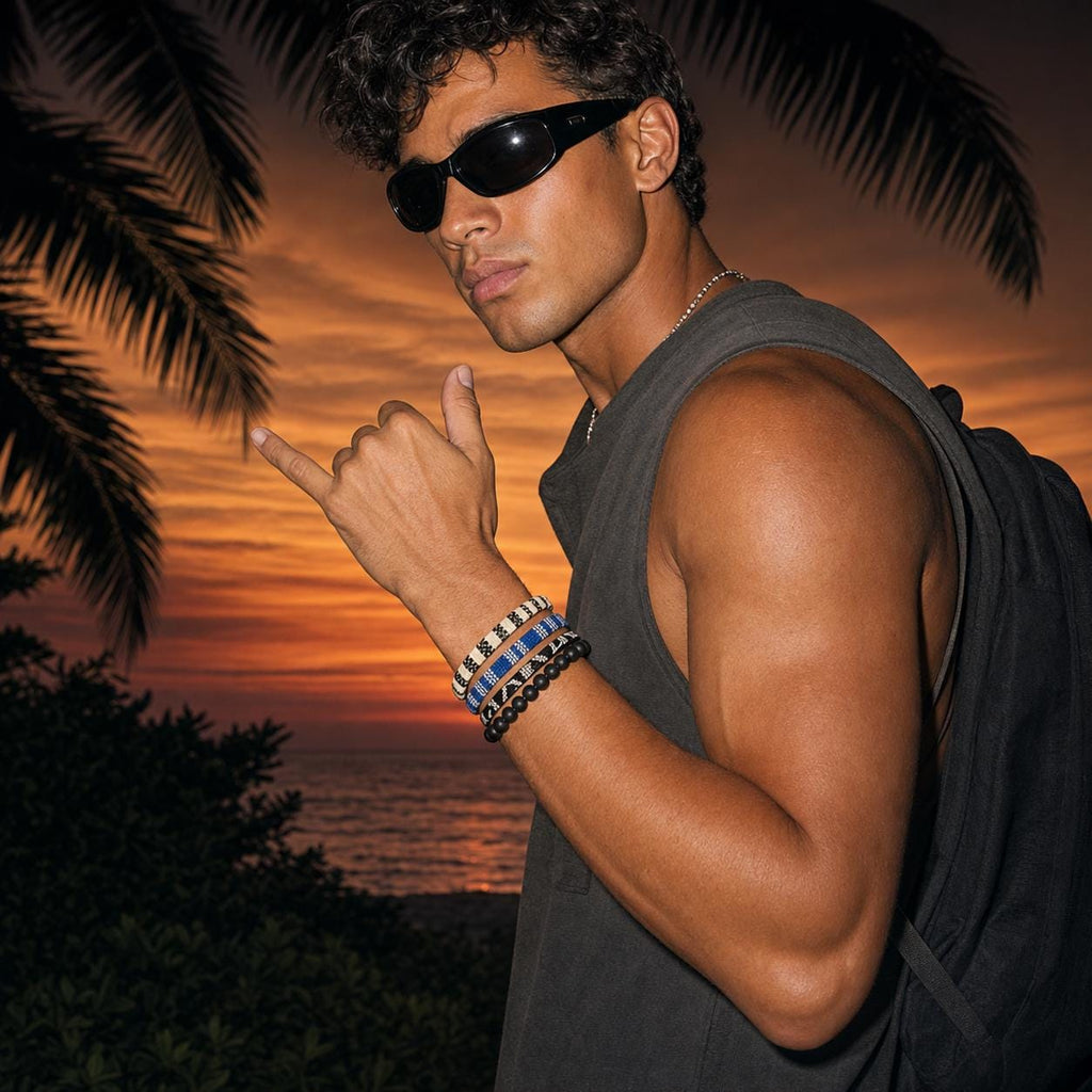 May include: A set of four bracelets worn on the wrist, featuring three woven bands with geometric patterns in black, white, and blue, alongside one bracelet composed of smooth, matte black spherical beads. The bracelets are worn together.