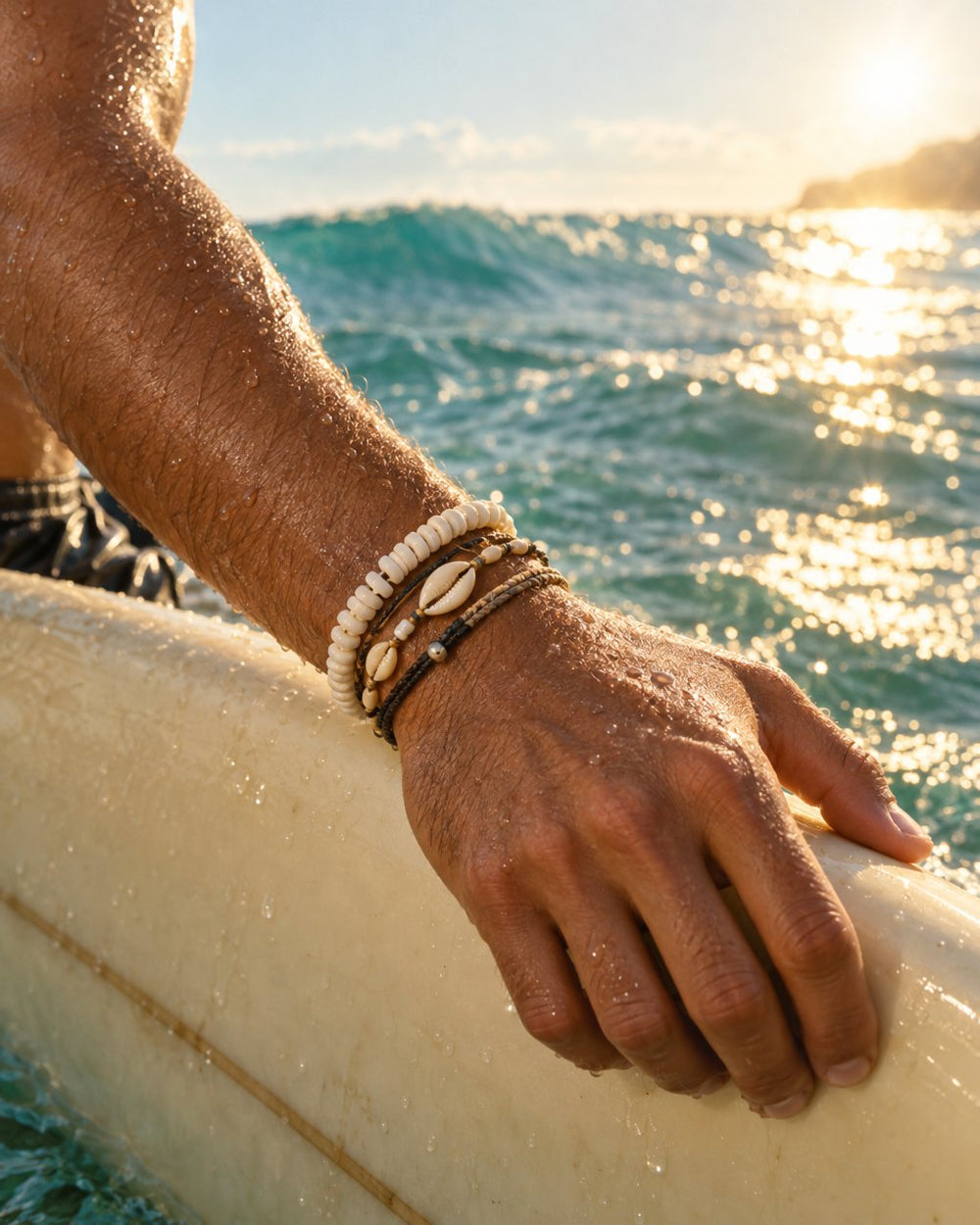 Shell and puka bracelets on a surfer's wrist resting on his board